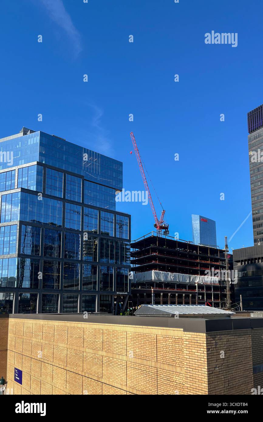 Una gru sta lavorando su un edificio nel mezzo di una città. Il cielo è limpido e blu, e il sole splende brillantemente Foto Stock Una gru sta lavorando su un edificio nel mezzo di una città. Il cielo è limpido e blu, e il sole splende brillantemente Foto Stock