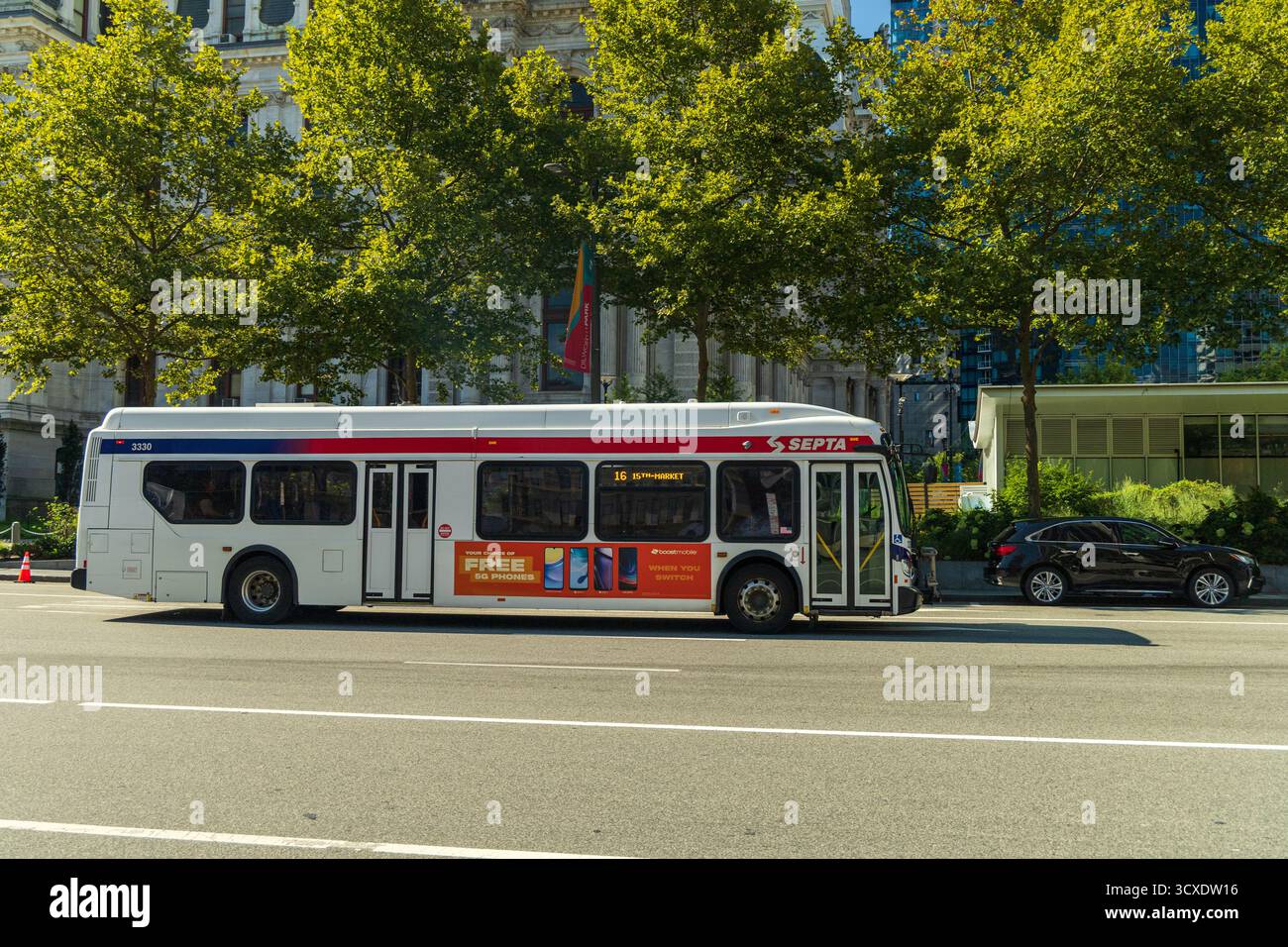 Un grande autobus bianco con una striscia rossa e una striscia blu sul lato. L'autobus e' su una strada con un'auto dietro di essa Foto Stock Un grande autobus bianco con una striscia rossa e una striscia blu sul lato. L'autobus e' su una strada con un'auto dietro di essa Foto Stock