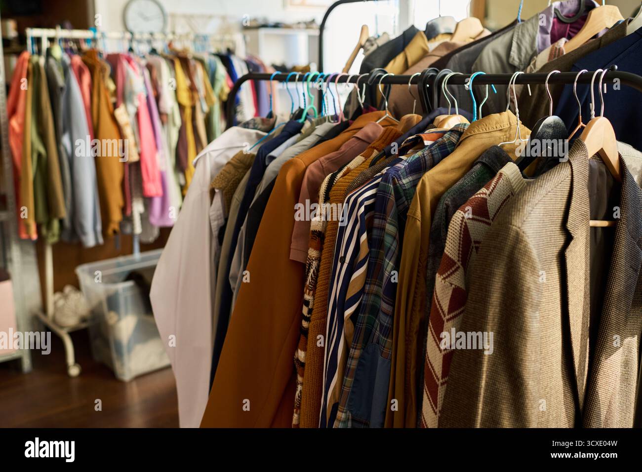 Appendiabiti che espongono capi vintage assortiti appesi nel negozio di abbigliamento, vari stili e tessuti visibili, sfondo con scaffali aggiuntivi riempiti di abiti usati Foto Stock