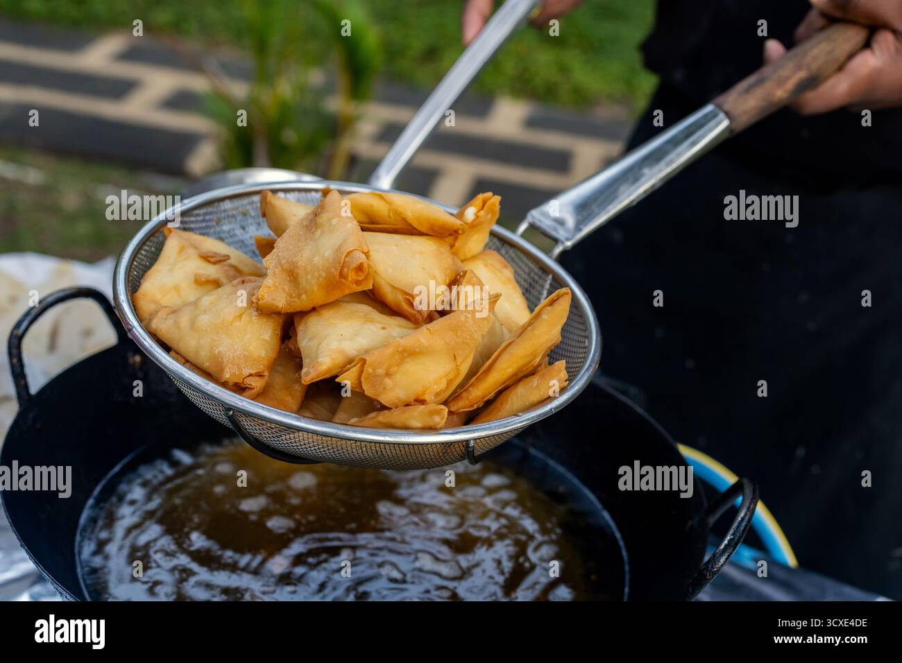 Samosas appena fritti vengono prelevati dall'olio caldo in un filtro metallico Foto Stock