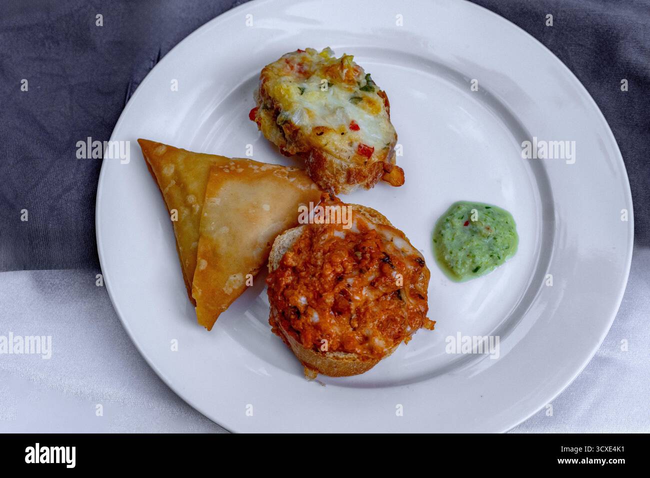 Delizioso piatto di antipasti con samosa, bruschette e una vivace salsa verde Foto Stock