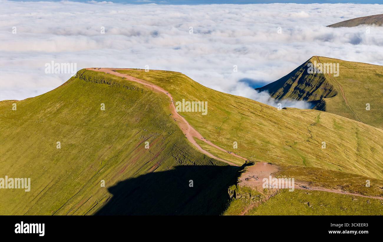 Escursionisti che camminano sulla cima della montagna Pen-y-fan sopra uno strato di nebbia e nuvole Foto Stock