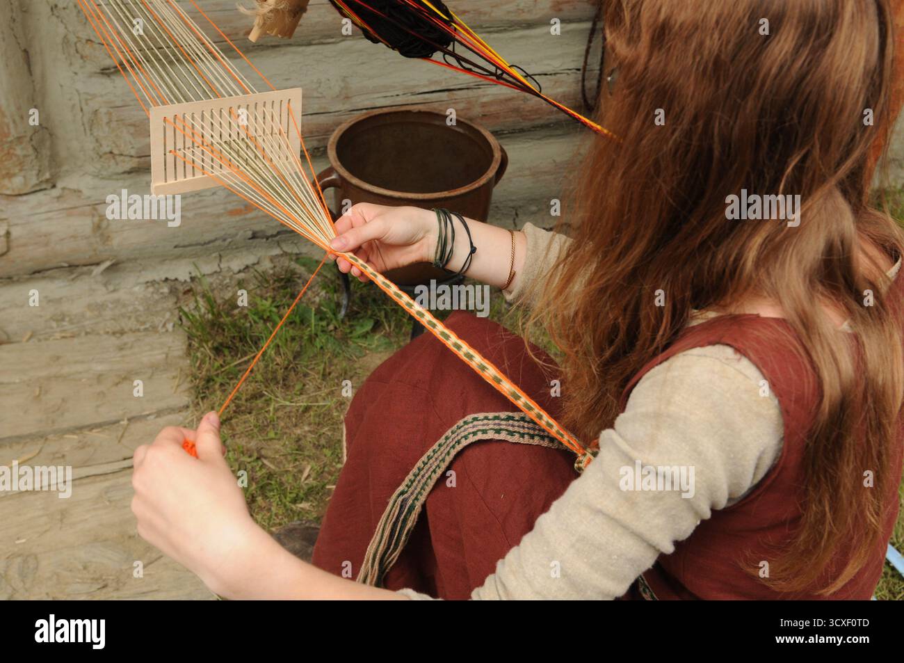 Donna in costume altomedievale che tessera una banda decorativa durante un evento di storia vivente presso il museo all'aperto Karpacka Troja di Trzcinica vicino a Jasło, Foto Stock