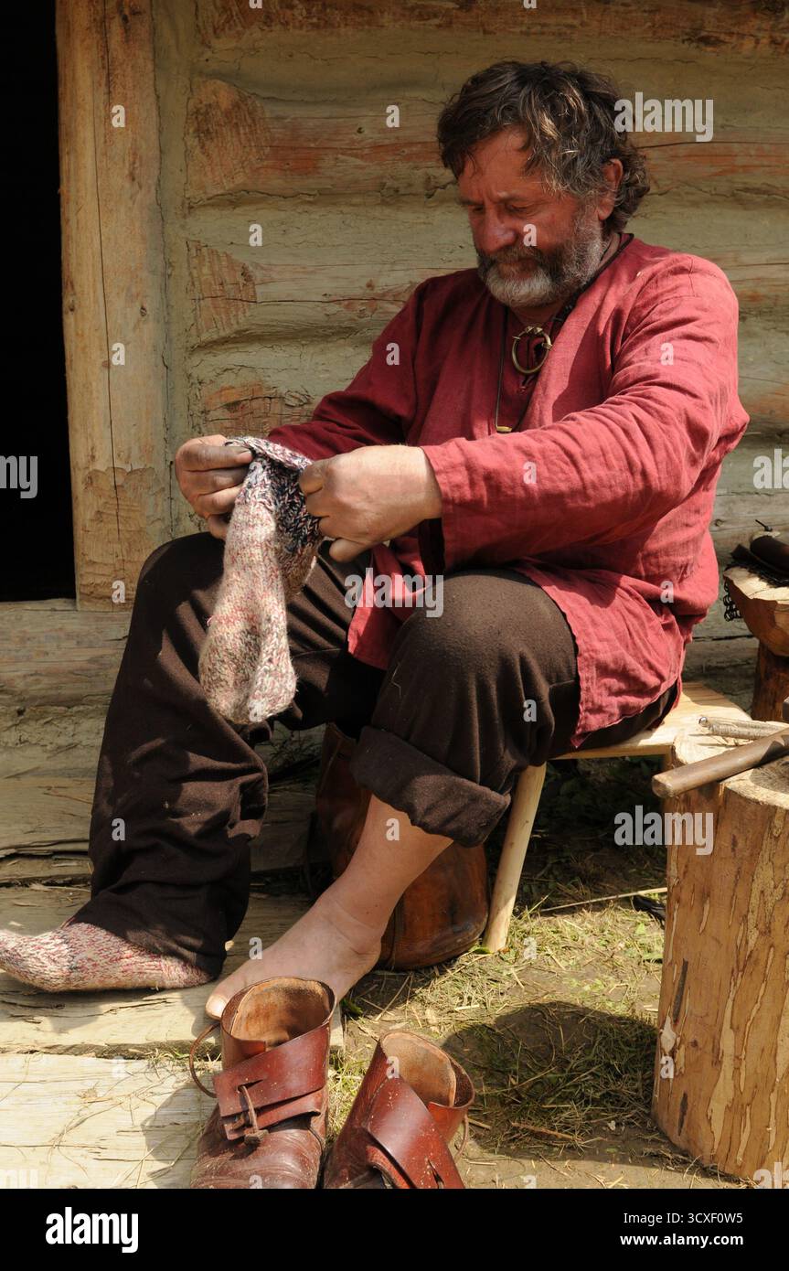 Rievocatore storico in costume del primo medioevo seduto accanto a una capanna di legno durante un evento di storia vivente presso il museo all'aperto Karpacka Troja di Trzcinic Foto Stock