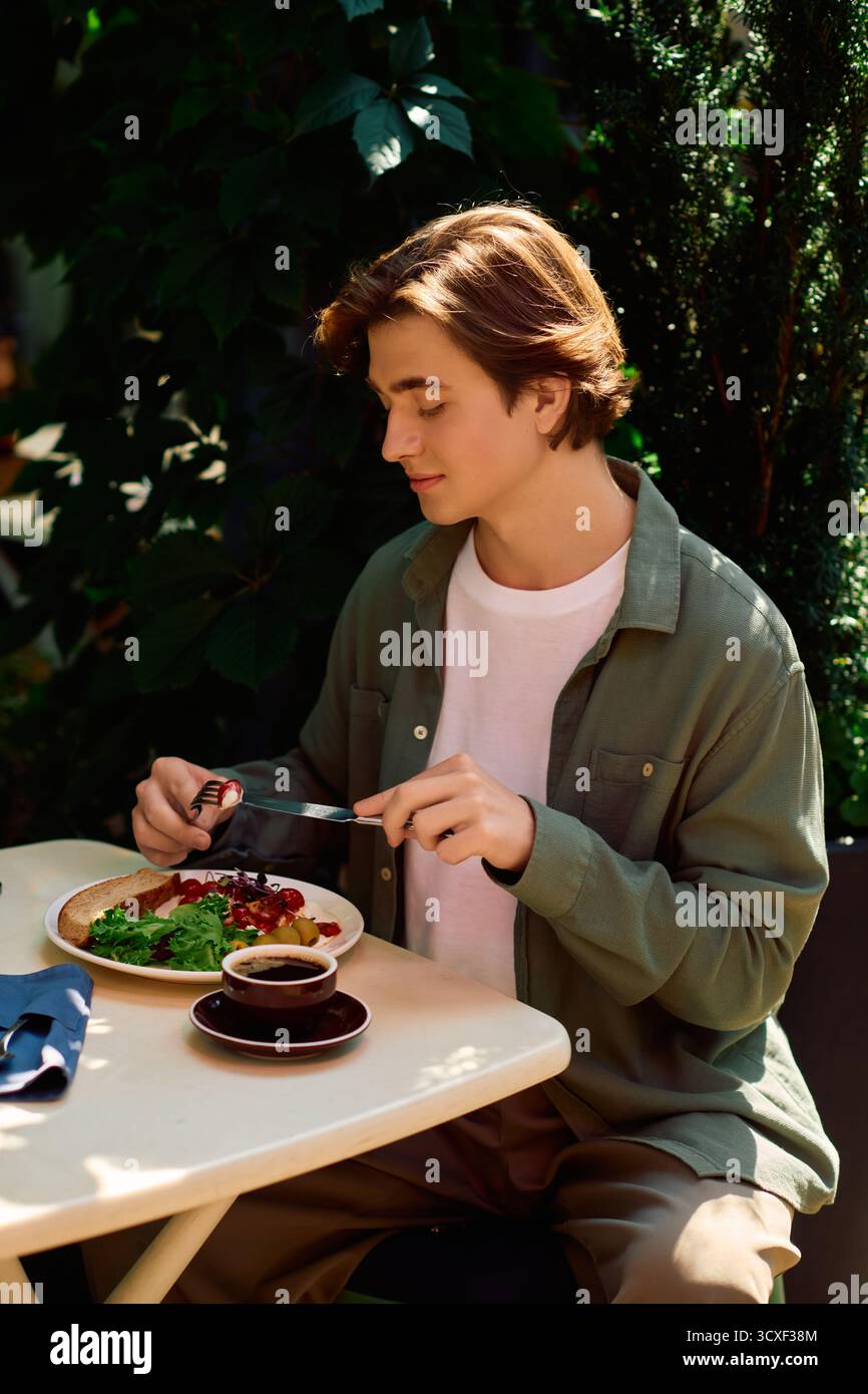 Un giovane con una camicia verde oliva assaggia il suo pasto in un bar alla moda, immerso nel momento. Foto Stock