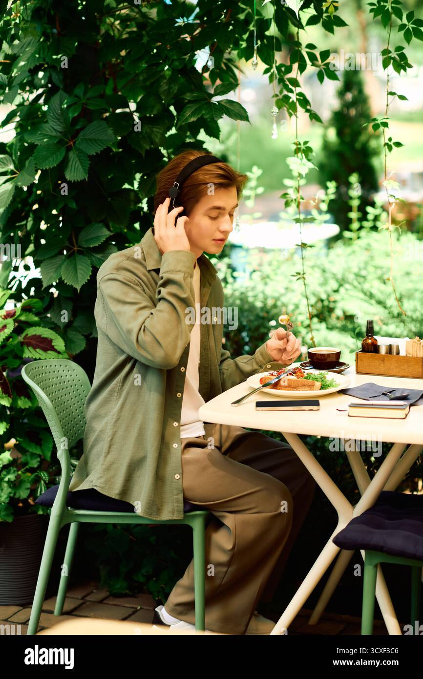 Giovane uomo con una camicia verde oliva che gusta il suo pasto seduto in un elegante caffè. Foto Stock