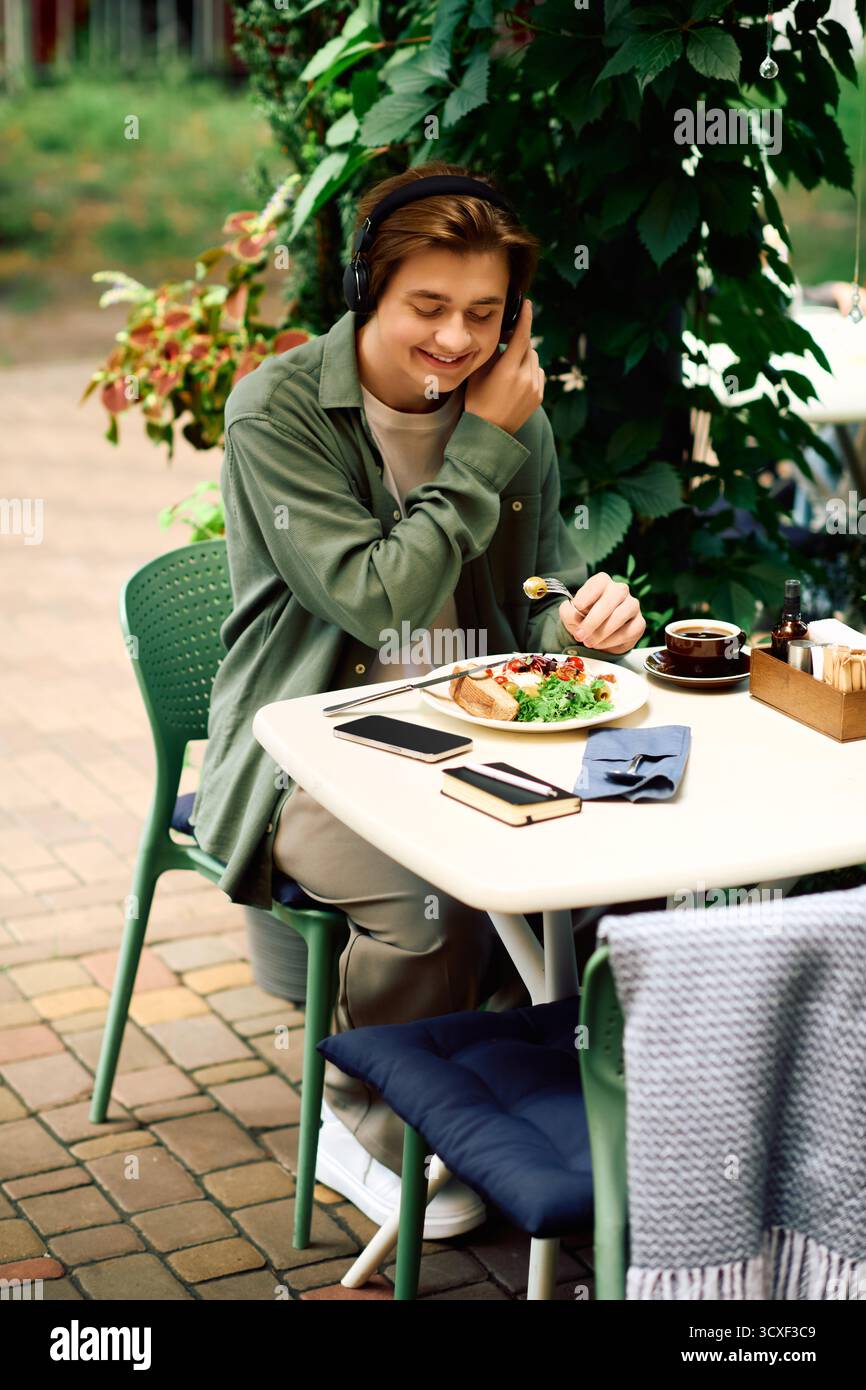 Un giovane uomo indossa una camicia verde oliva e sorride mentre mangia il suo pasto in un elegante bar. Foto Stock