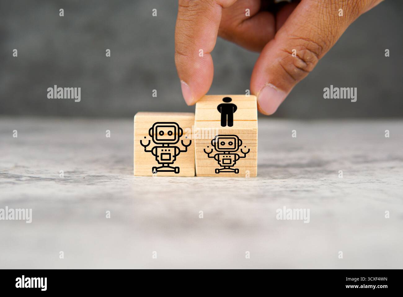 Mano umana che posiziona cubi di legno con icone di robot e umani affiancati, simboleggiando l'intelligenza artificiale, la collaborazione umana, l'automazione. Foto Stock