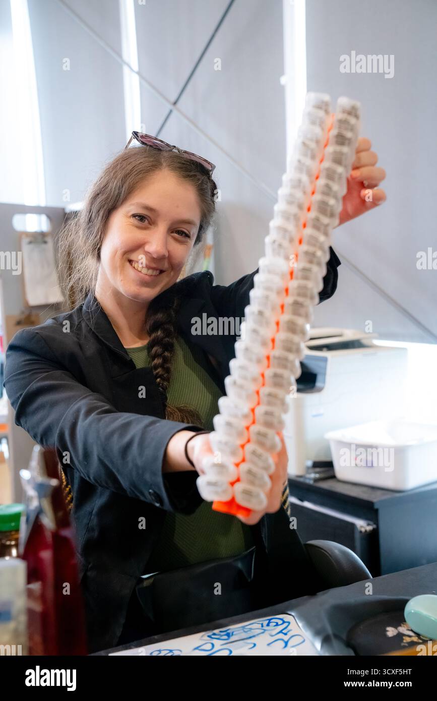 Una donna sorride mentre tiene una fila di gabbie di api regine durante una dimostrazione di apicoltura presso la Dancing Bee Farm, parte di un programma di educazione all'apicoltura Foto Stock