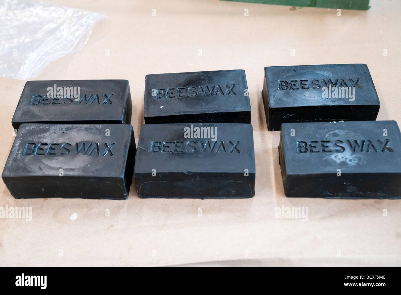 Pila di barre nere di cera d'api etichettate "cera d'api" su un tavolo di lavoro, che rappresentano i prodotti naturali di cera utilizzati nella produzione di candele e cosmetici Foto Stock