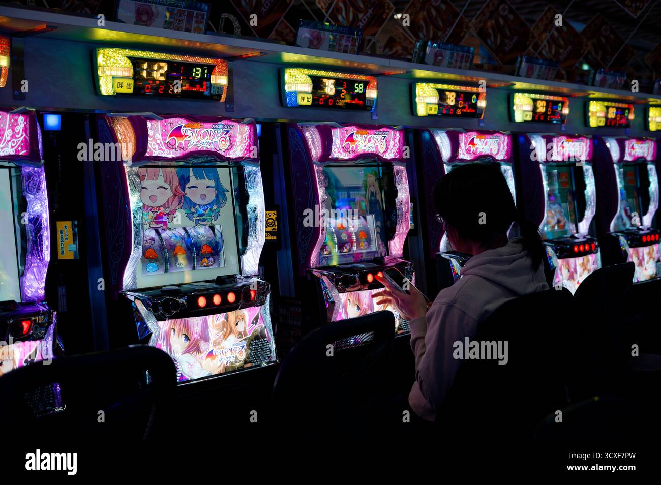 Una donna gioca in una fila di macchine pachinko luminose a Osaka Foto Stock