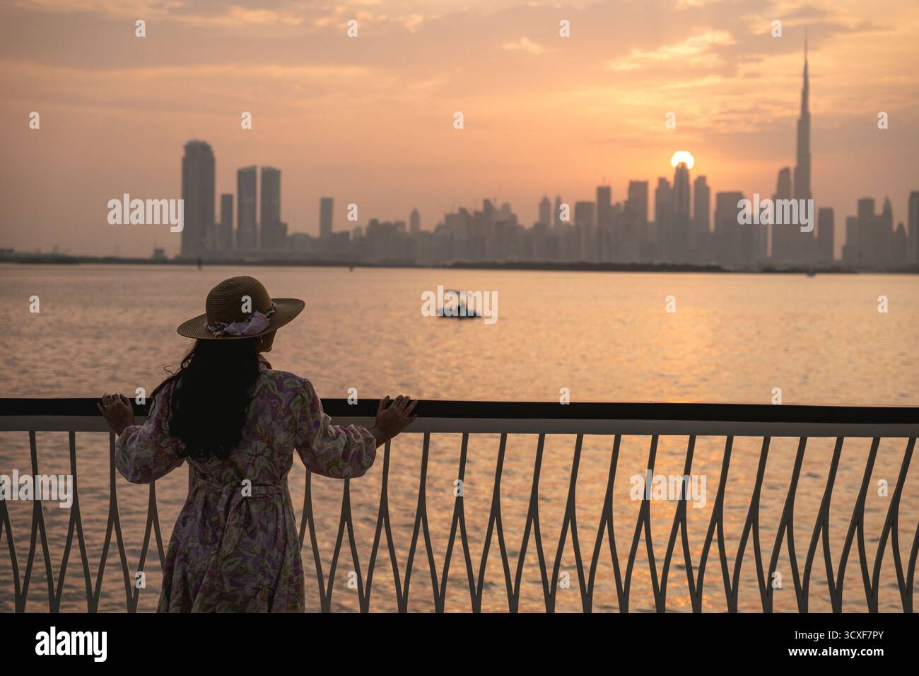 Silhouette di moderni grattacieli contro il cielo del tramonto con barca a vela sull'acqua nello skyline della città di Dubai Foto Stock