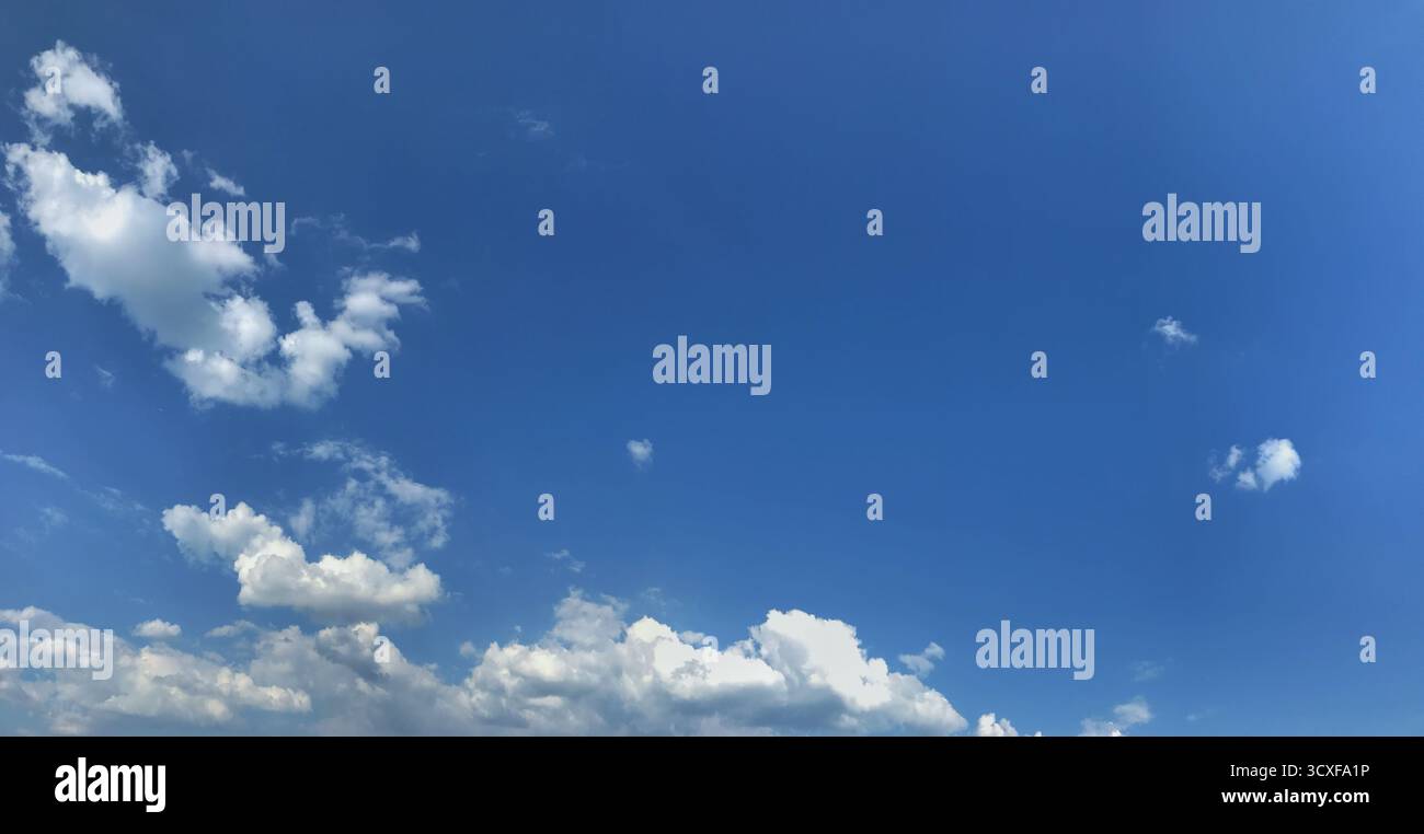 Un vasto cielo blu con nuvole bianche e soffici sparse su tutto, creando una luminosa vista panoramica. Questa immagine evoca sentimenti di serenità e libertà infinita, Foto Stock