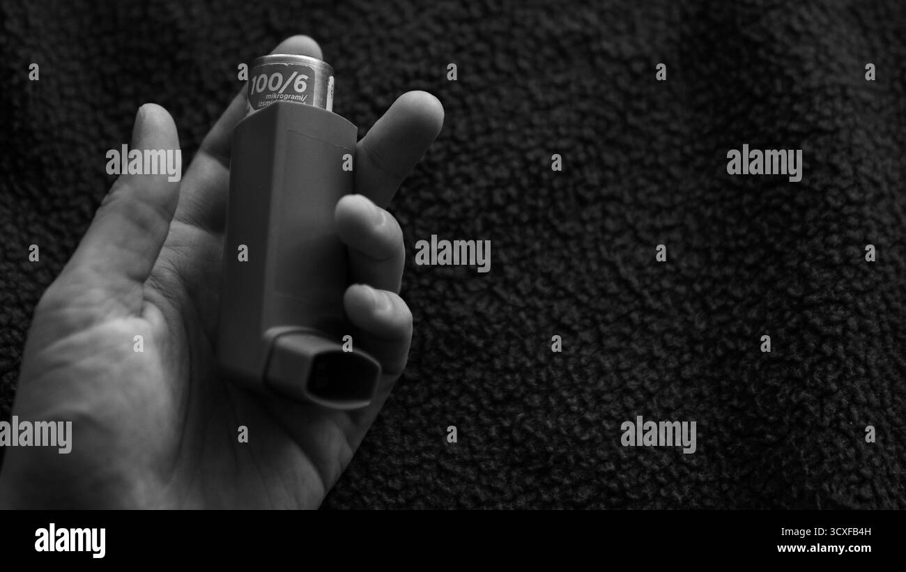 Mano che tiene l'inalatore per asma su sfondo scuro Foto Stock