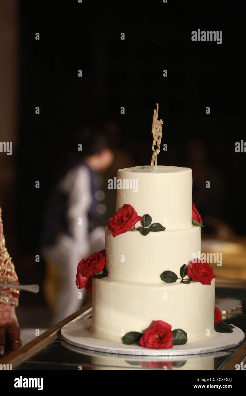 Un'incredibile torta nuziale bianca a tre piani decorata con rose rosse fresche, che simboleggia eleganza, amore e celebrazioni senza tempo. Foto Stock