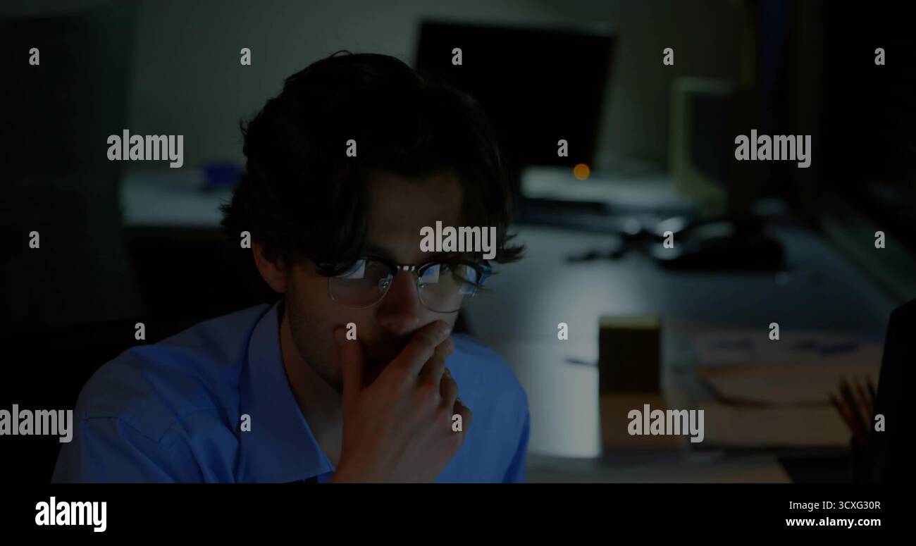 Appoggiando il mento sul lavoratore a mano osservando i monitor del computer in ufficio con carta e portamatite Foto Stock