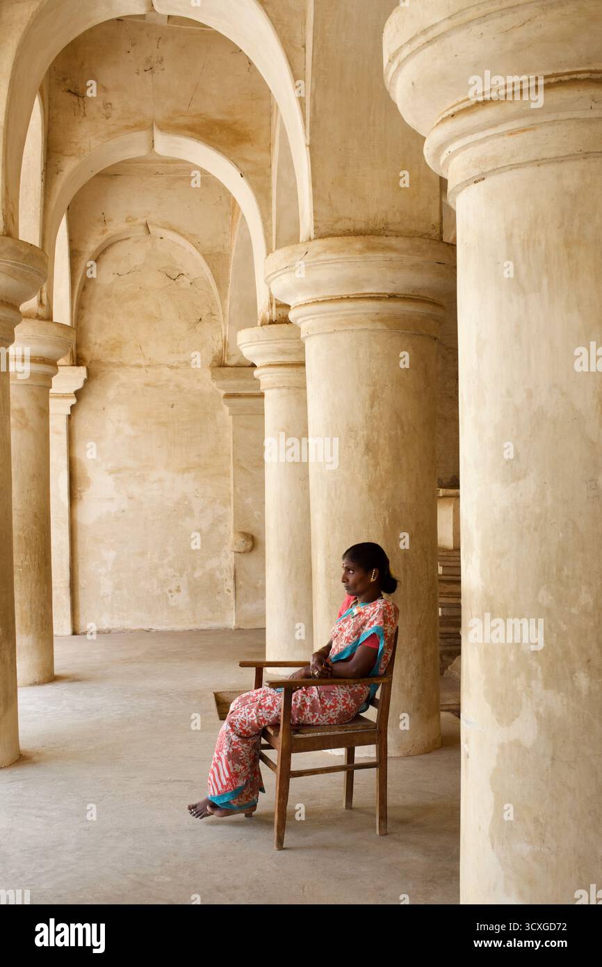Donna seduta sotto gli archi a volta del Palazzo Maratha di Thanjavur, Tamil Nadu, India, che mostra influenze indo-islamiche e maratha a strati. Foto Stock