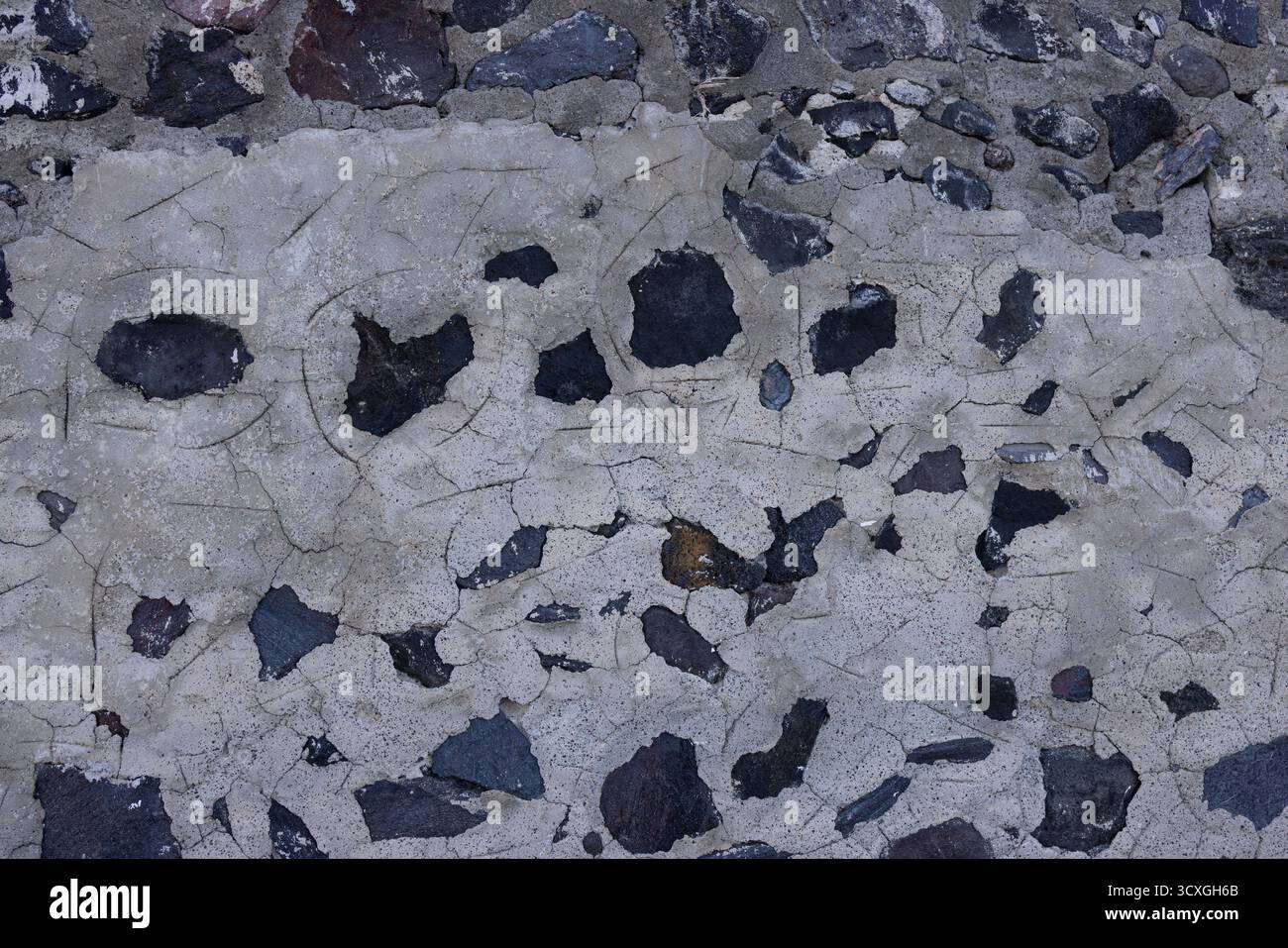 Primo piano della vecchia parete di pietra del Mediterraneo con argilla chiara incrinata e rocce vulcaniche Foto Stock