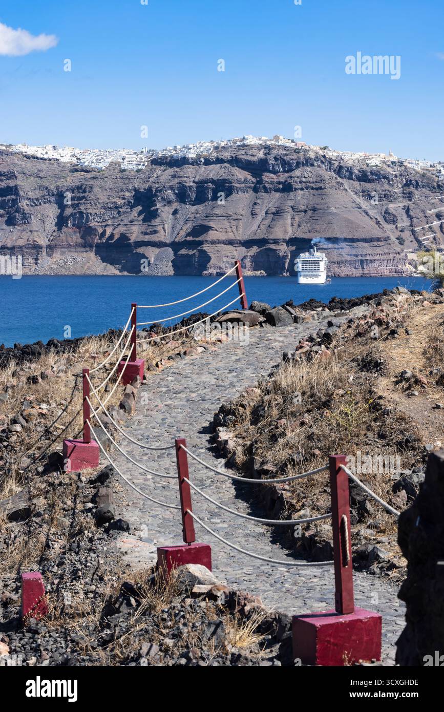 Sentiero vulcanico panoramico con barriera di corda che si affaccia sulla caldera di Santorini, sulla nave da crociera e sul lontano villaggio di Fira Foto Stock