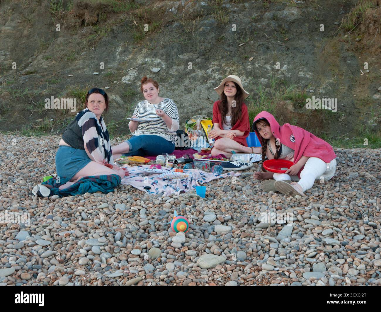 Le famiglie possono godersi un picnic sulla spiaggia di ciottoli sotto le spettacolari scogliere del Dorset Foto Stock