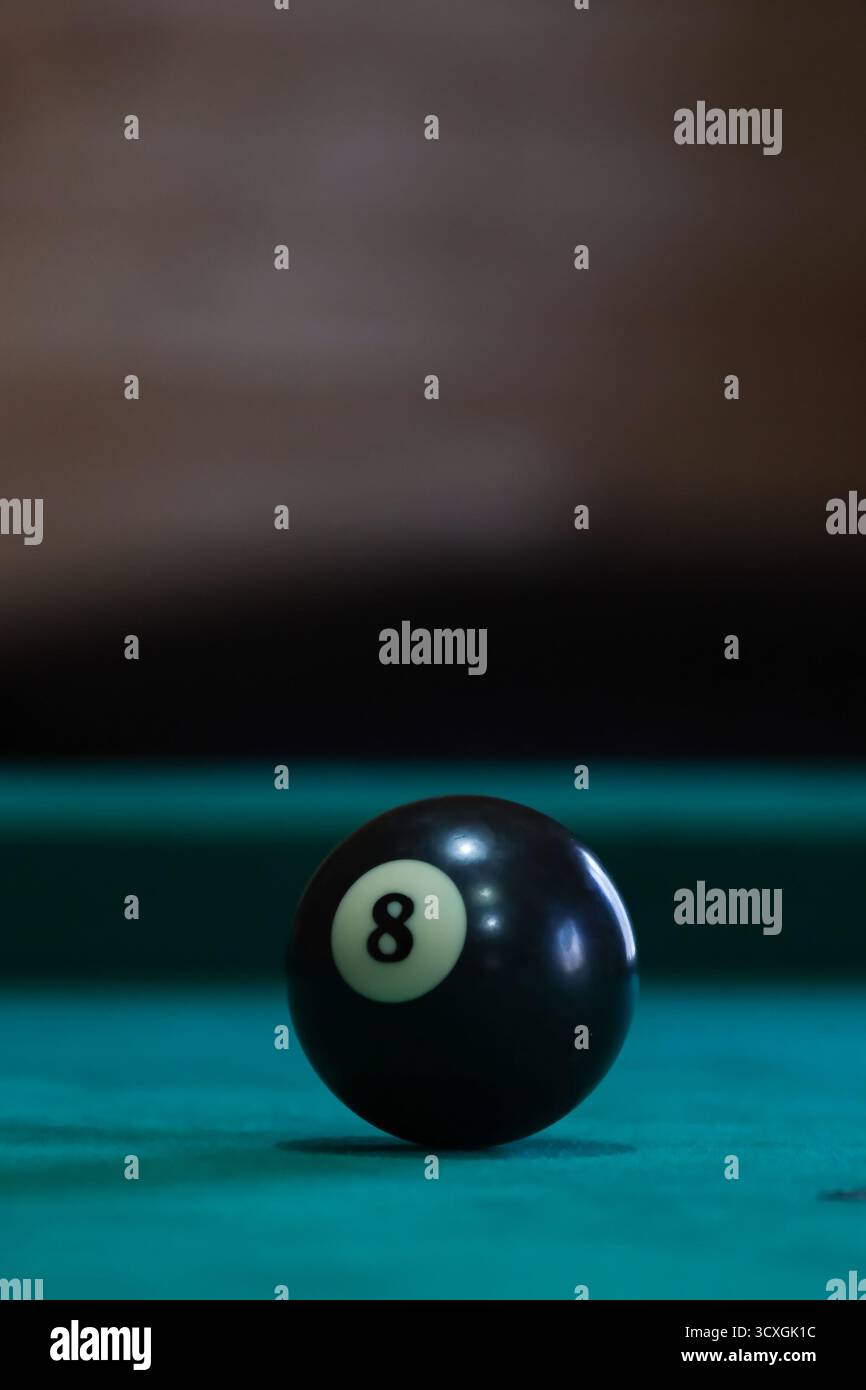 Palla nera 8 sul tavolo da biliardo verde sotto luce soffusa, simbolo di concentrazione e decisione nel biliardo o nel concetto di strategia di gioco Foto Stock
