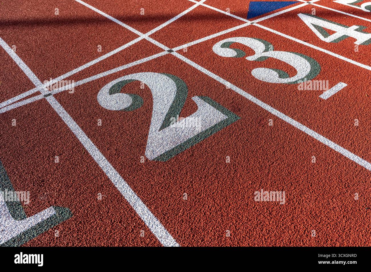 Foto ravvicinata della pista da corsa all'aperto, numeri bianchi due, 2, 3, con ombra verde su una nuova pista rossa con linee bianche. Foto Stock