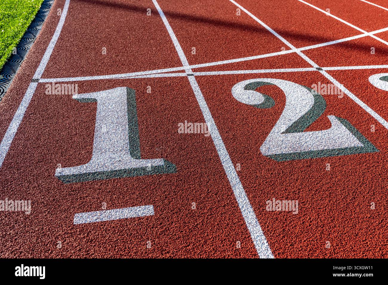 Foto ravvicinata della pista da corsa all'aperto con numeri bianchi uno due, 1, 2, con ombra verde su una nuova pista rossa con linee bianche. Foto Stock