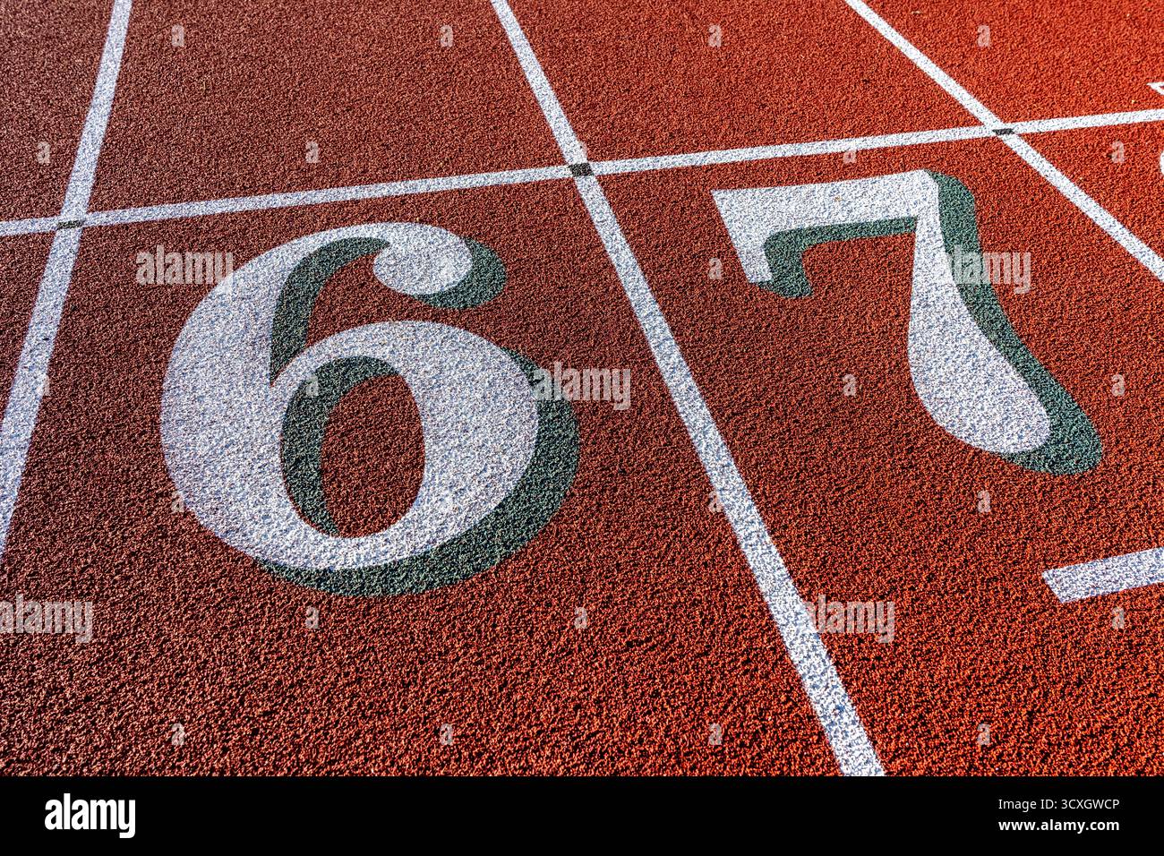 Foto ravvicinata della pista da corsa all'aperto, numeri bianchi sei, 6, 7, con ombra verde su una nuova pista rossa con linee bianche. Foto Stock