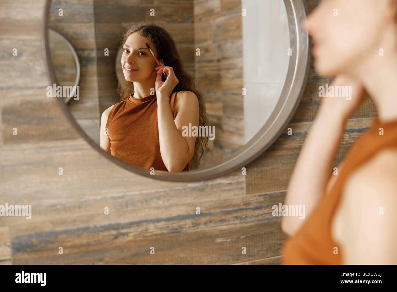 Una donna che applica il suo trucco nel riflesso di un moderno specchio per il bagno Foto Stock