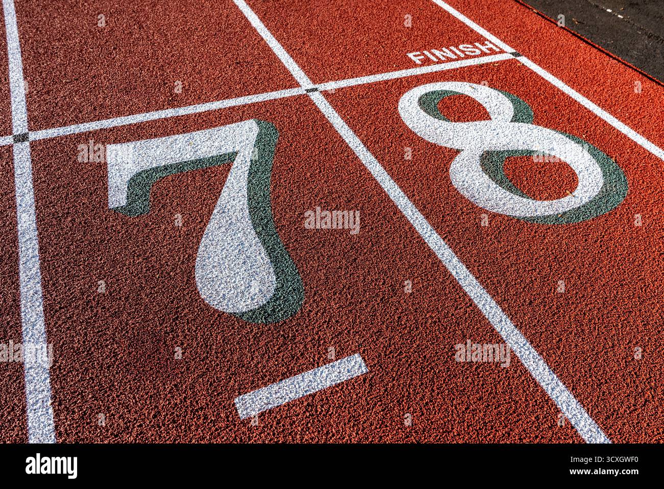 Foto ravvicinata della pista da corsa all'aperto, numeri bianchi sette otto, 7, 8, con ombra verde su una nuova pista rossa con linee bianche. Foto Stock