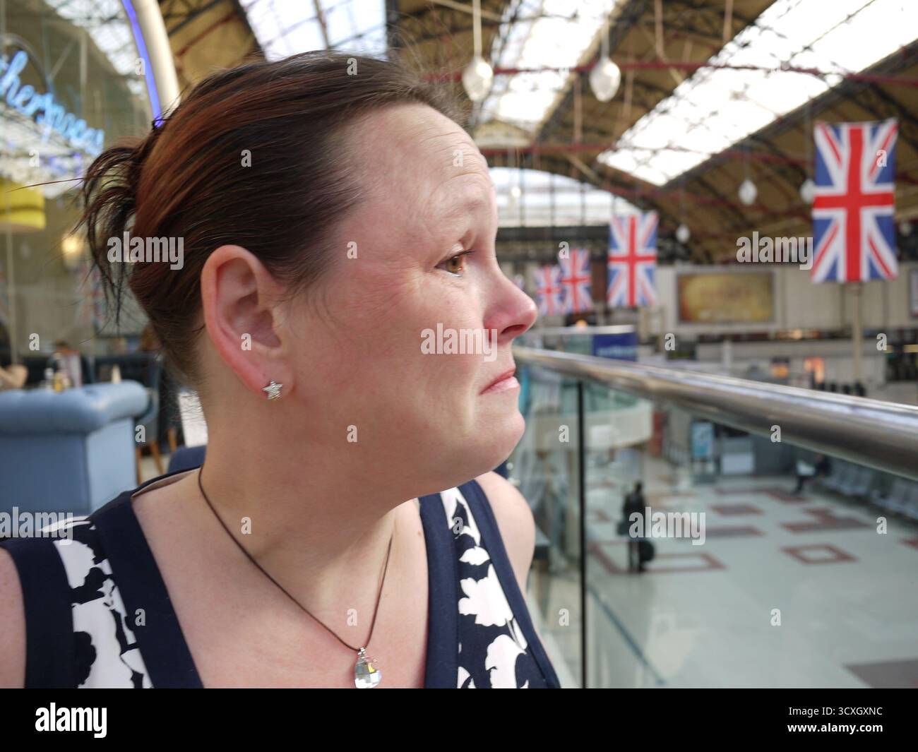 Donna alla stazione ferroviaria vittoriana con bandiere Union Jack sopra la testa Foto Stock
