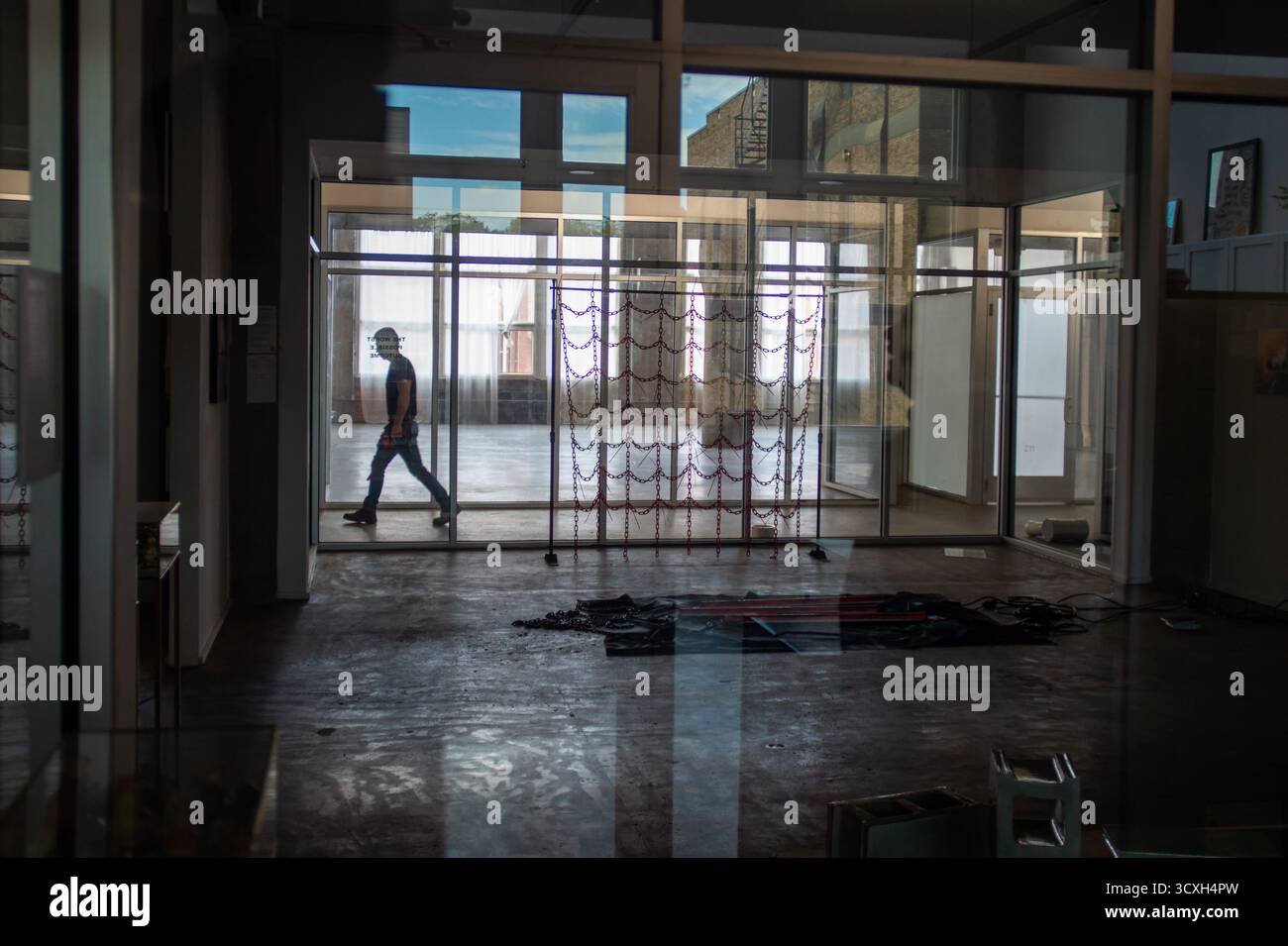 Architettura urbana: Una figura solitaria si muove attraverso uno spazio commerciale vuoto e moderno definito da una suggestiva griglia di vetro e luce. Ideale per persone vere Foto Stock