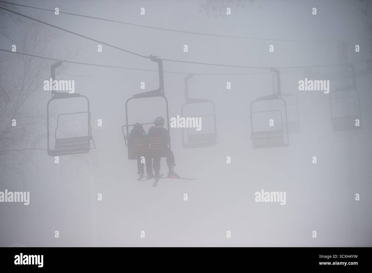 Suggestivo scenario invernale di una coppia in seggiovia attraverso fitta nebbia e neve. Bassa visibilità su un pendio nebbioso. Foto Stock