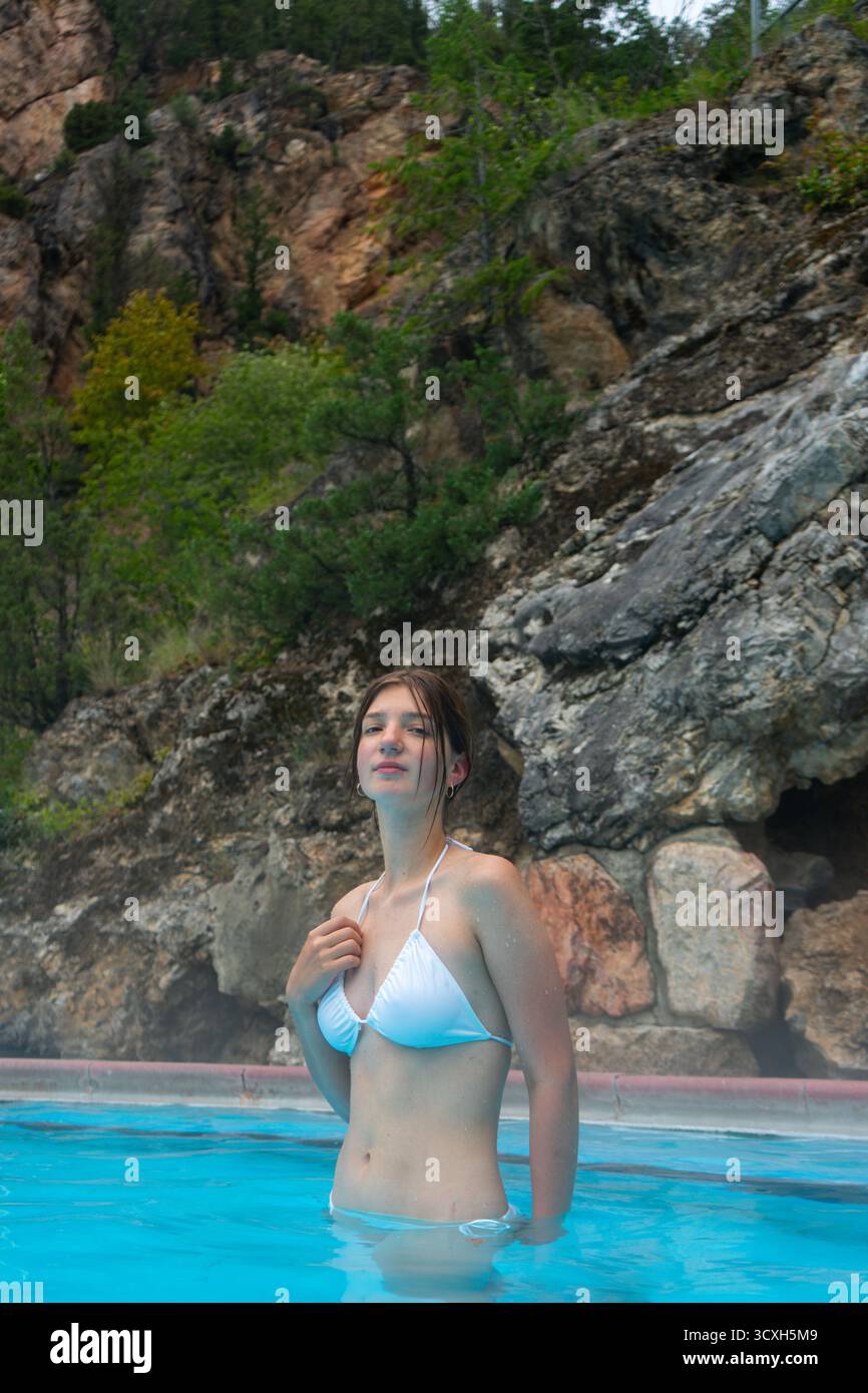Donna in costume da bagno che si rilassa nella piscina all'aperto con rocce alle sue spalle. Radium Hot Springs, British Columbia Foto Stock