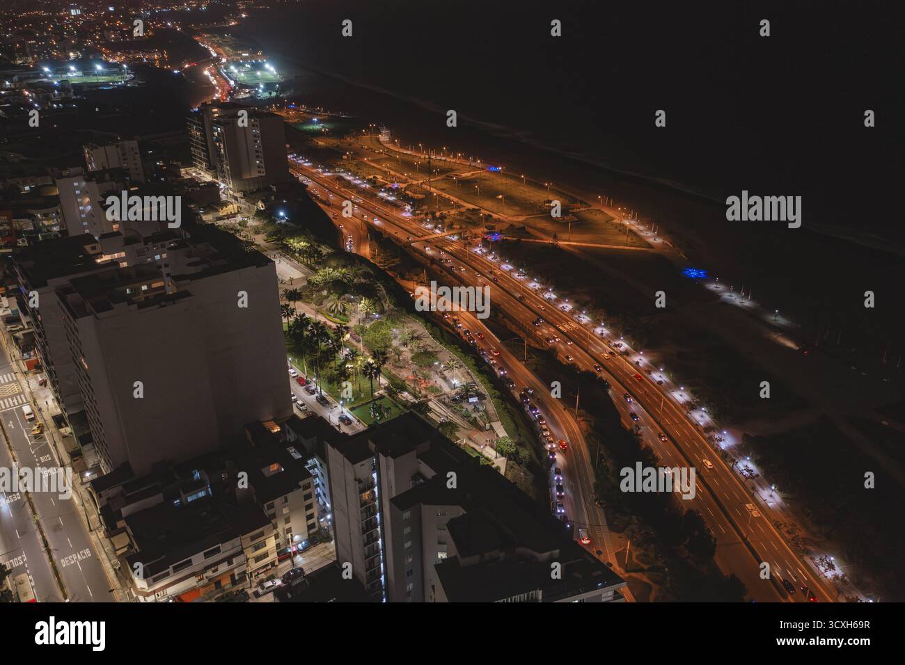 Panoramica aerea che cattura il traffico urbano notturno che scorre lungo un'autostrada costiera illuminata Foto Stock
