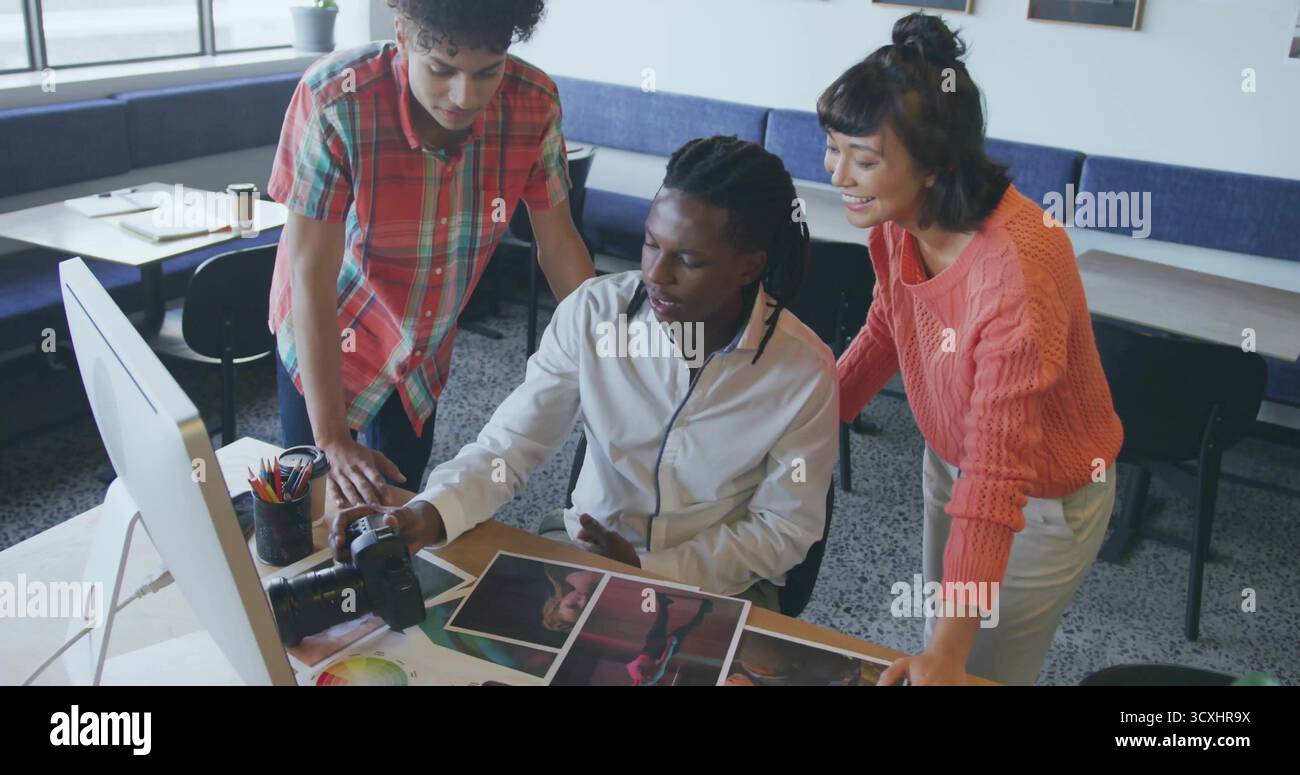 Rivedere tre colleghi che si riuniscono intorno alla scrivania in un moderno studio, con fotocamera DSLR e fotografie Foto Stock