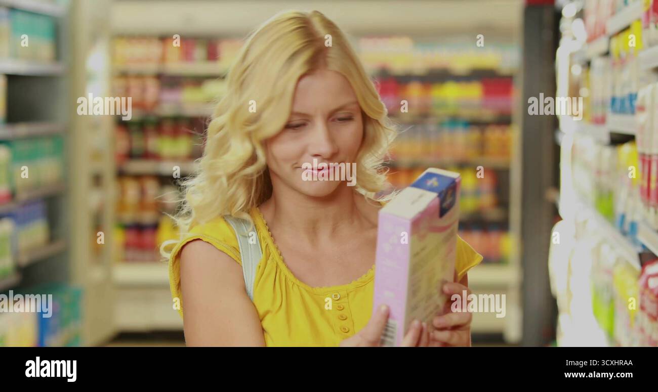 Esame di una donna che indossa un'etichetta di lettura della scatola con la parte superiore del serbatoio gialla nella corsia della spesa, con cinghia per sacchetti Foto Stock