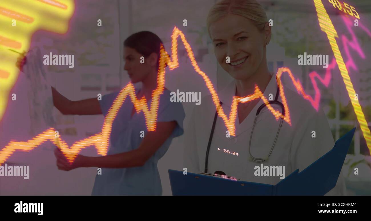 Medico sorridente che tiene in camera gli appunti e lo stetoscopio, con un collega che scrive sulla lavagna Foto Stock