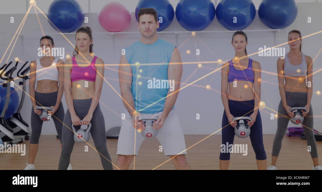 Uomo in cima turchese che solleva kettlebell in palestra, con palle di stabilità, biciclette e nodi sovrapposti Foto Stock