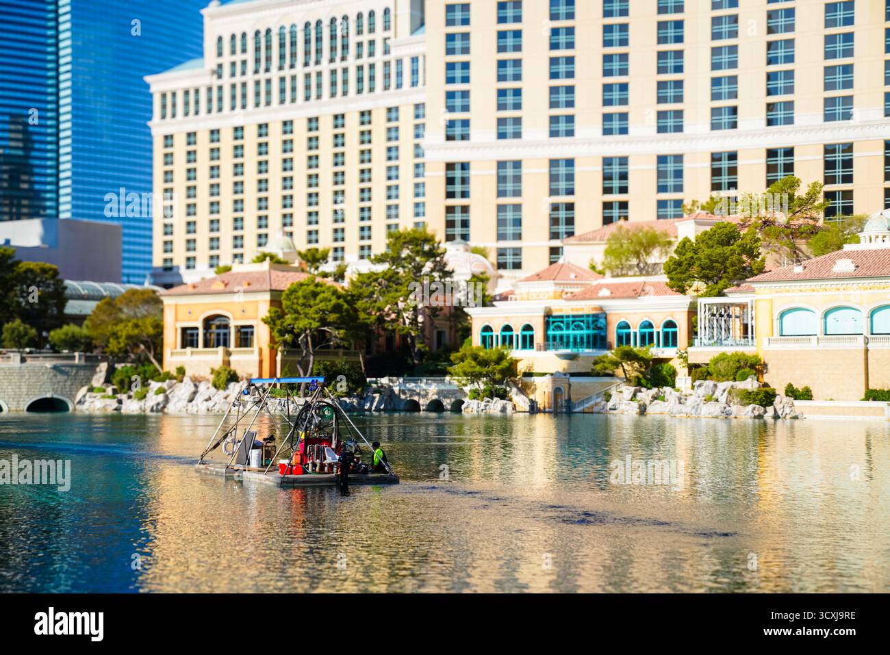 I lavoratori a bordo di una piccola chiatta di manutenzione gestiscono le attrezzature nel lago Bellagio con la facciata e i riflessi visibili dietro di loro Foto Stock