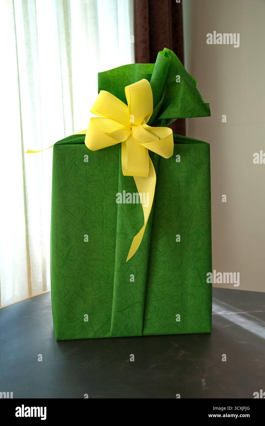 Confezione regalo in carta verde con nastro giallo sul tavolo Foto Stock