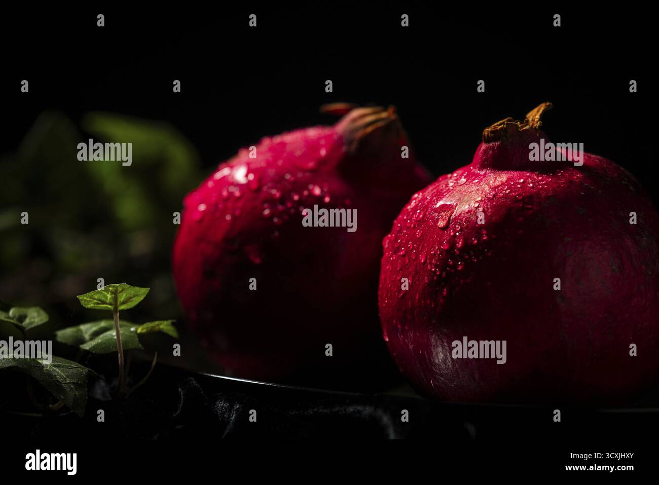 Due melograni con gocce d'acqua in un'atmosfera buia Foto Stock