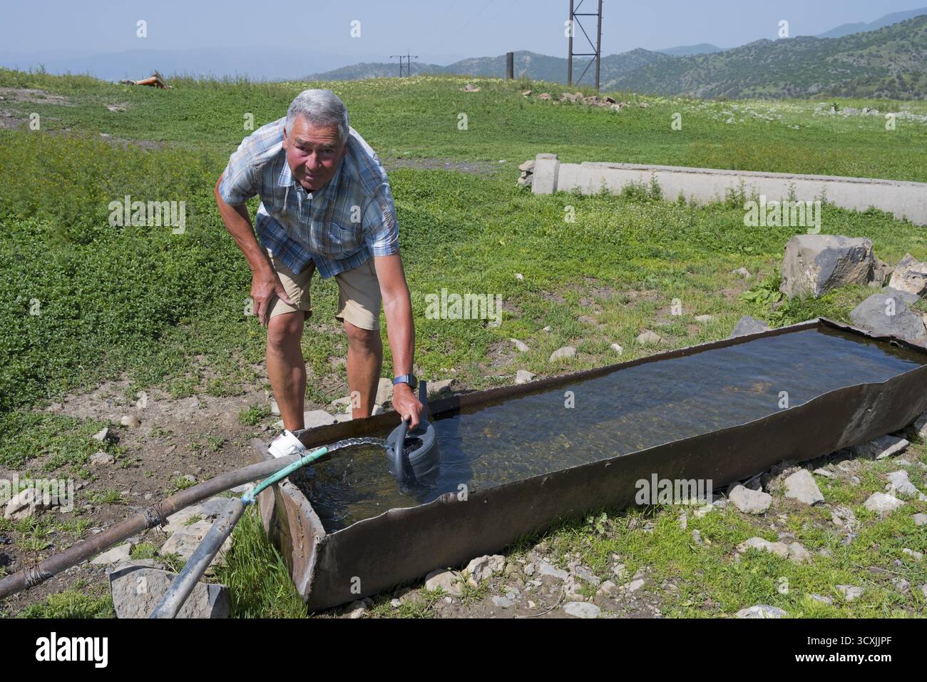 Un uomo che recupera acqua con una bomboletta in un paesaggio naturale montagnoso, un uomo che si riempie di acqua potabile in un pozzo d'acqua, vicino a Jermuk, Jermu Foto Stock