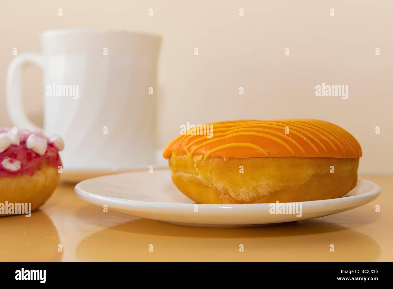 Ciambella smaltata arancione su piatto bianco con tazza di caffè su sfondo beige Foto Stock