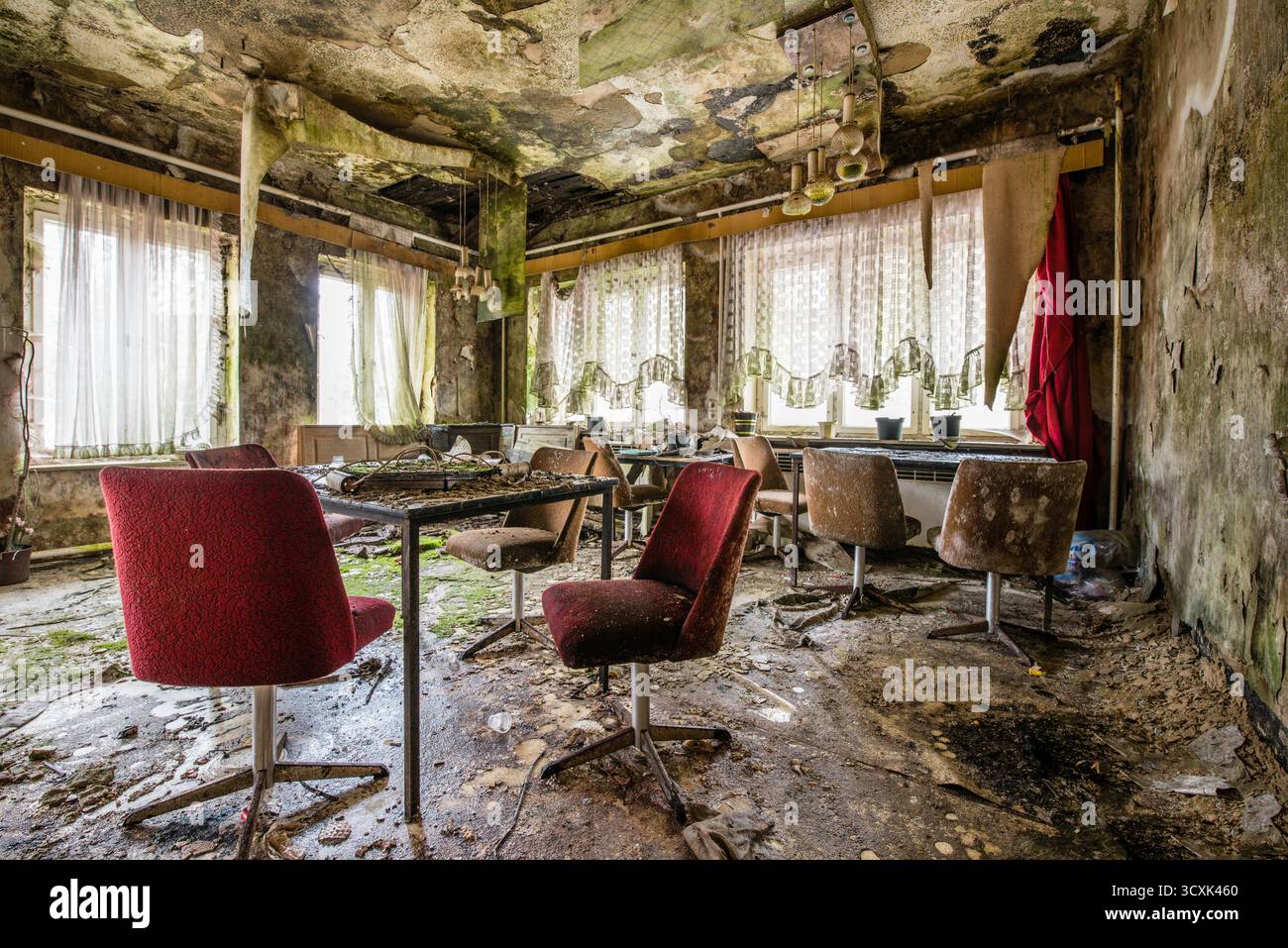 Sala da pranzo abbandonata con sedie rosse e pareti in decadenza Foto Stock