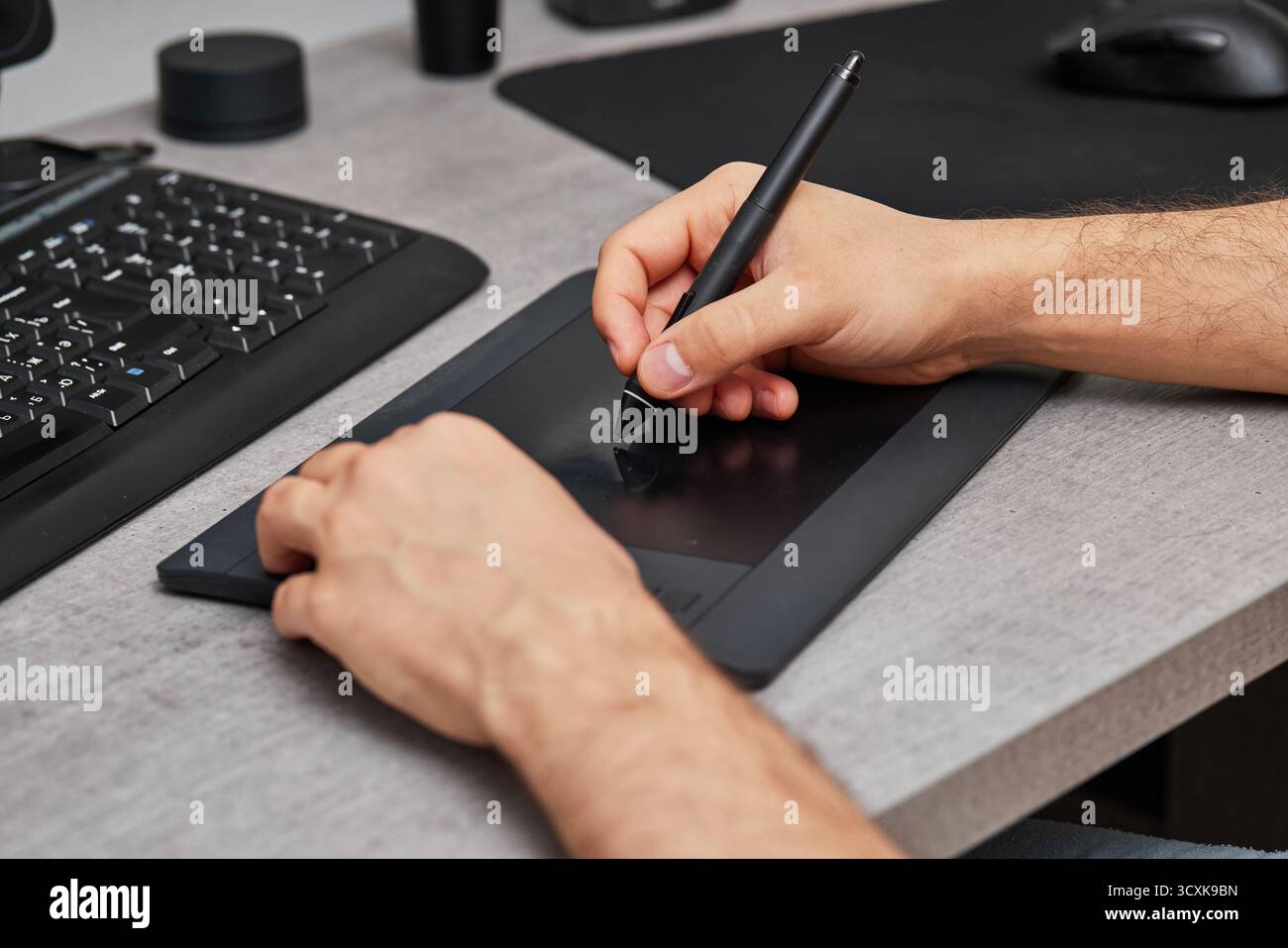 mani maschili che disegnano e ritoccano l'immagine sul computer pc, utilizzando un tablet grafico digitale e una penna stilo alla scrivania dell'ufficio. Foto Stock