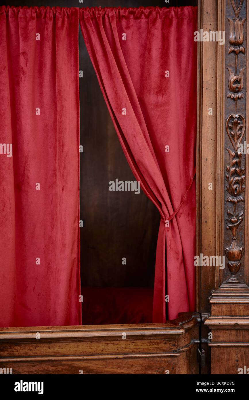 Tenda rossa e dettagli in legno intagliato della chiesa confessionale, simbolo di fede e spiritualità. Foto Stock