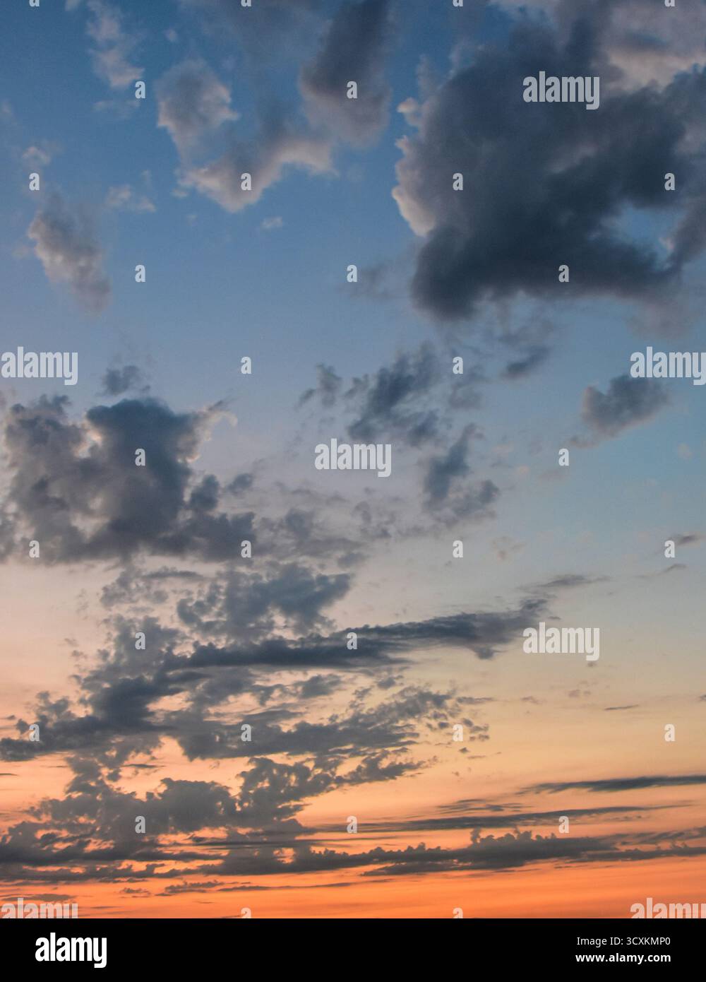 La calda luce del tramonto splende dolcemente attraverso le nuvole delicate in un cielo pastello e luminoso, creando un magico momento naturale. Foto Stock