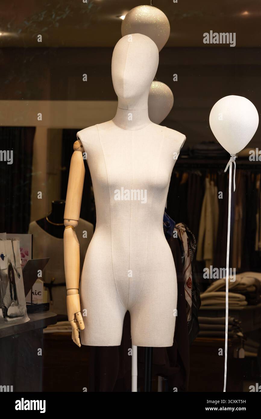 Elegante manichino sartoriale con braccio in legno si stende graziosamente in una boutique di moda circondata da abiti eleganti e riflessi di luce soffusa. Foto Stock