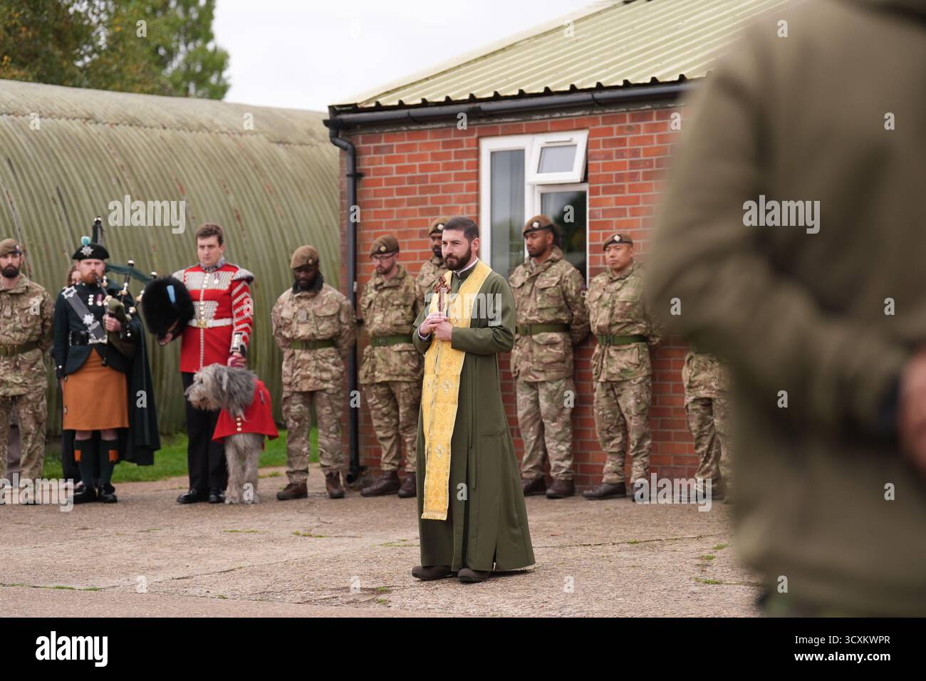 Un padre ucraino offre una benedizione e preghiere durante una parata di addio per i soldati ucraini in un campo di addestramento dell'esercito britannico nell'Inghilterra orientale, dove sono stati sottoposti ad addestramento di combattimento con le guardie irlandesi come parte dell'operazione Interflex guidata dal Regno Unito. Data foto: Mercoledì 15 ottobre 2025. Foto Stock